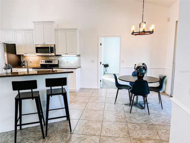 kitchen with decorative backsplash, stainless steel appliances, light tile patterned floors, a notable chandelier, and white cabinetry