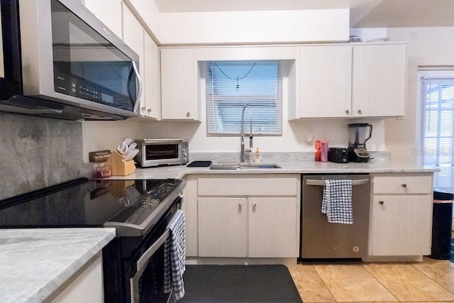 kitchen with a toaster, appliances with stainless steel finishes, light countertops, white cabinetry, and a sink