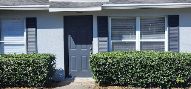 view of exterior entry featuring stucco siding and a shingled roof