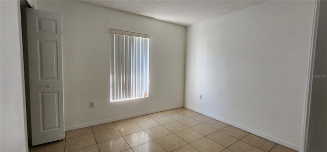 empty room with light tile patterned floors, baseboards, and a textured ceiling