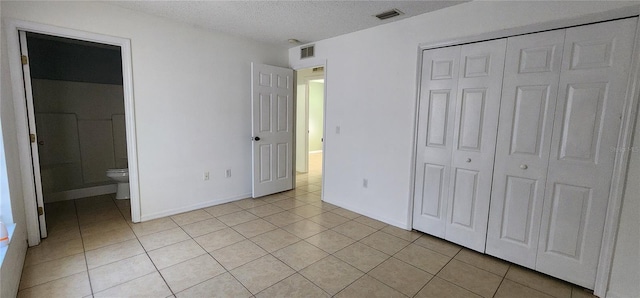 unfurnished bedroom with light tile patterned flooring, visible vents, a closet, and a textured ceiling