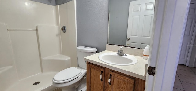 bathroom featuring toilet, a stall shower, a textured wall, tile patterned floors, and vanity