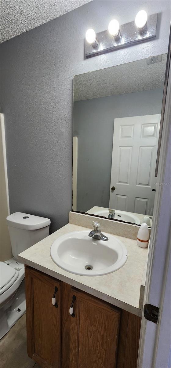 bathroom with a textured ceiling, toilet, vanity, and a textured wall