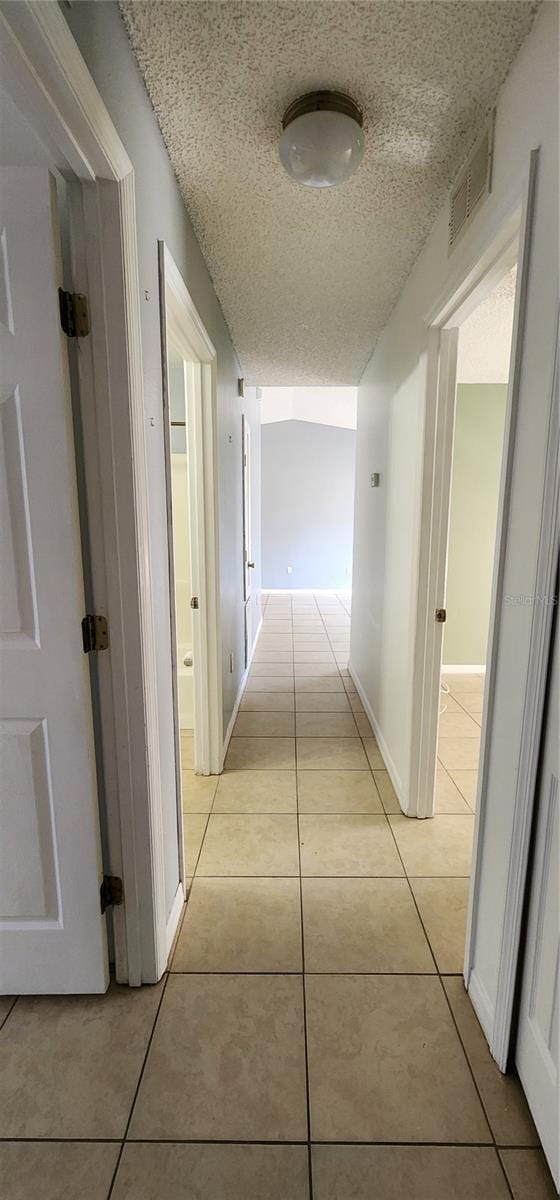 hallway with light tile patterned floors, visible vents, baseboards, and a textured ceiling