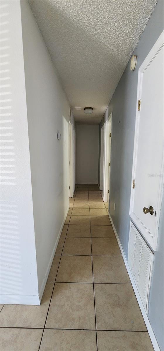 hallway featuring light tile patterned floors, visible vents, baseboards, and a textured ceiling