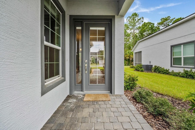 view of exterior entry with a yard and central air condition unit