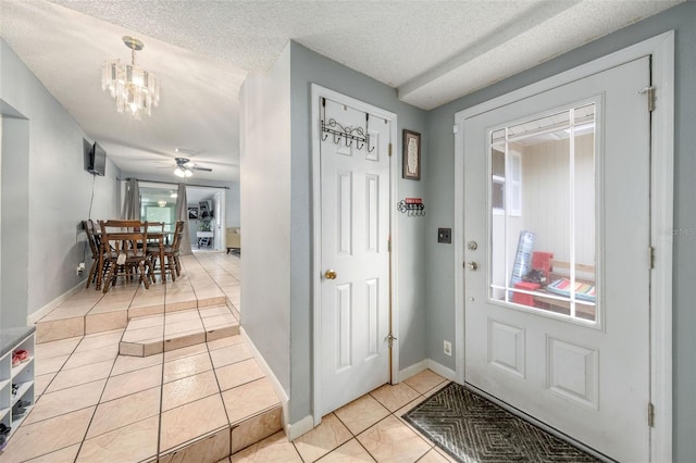 tiled foyer entrance featuring a textured ceiling and ceiling fan with notable chandelier