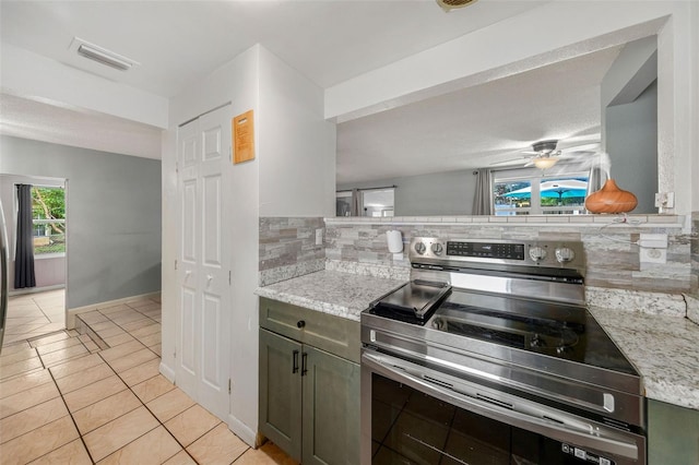 kitchen with light stone counters, backsplash, light tile patterned floors, ceiling fan, and stainless steel range with electric cooktop