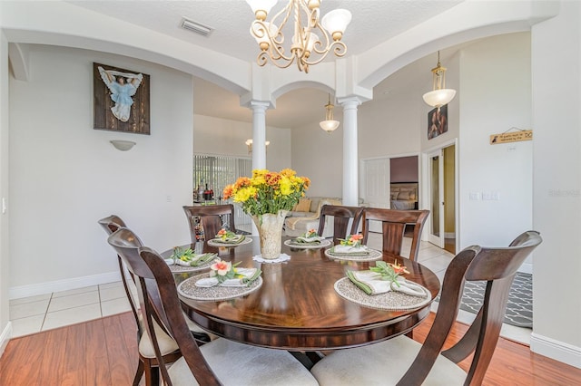 tiled dining area featuring a textured ceiling, a notable chandelier, and ornate columns