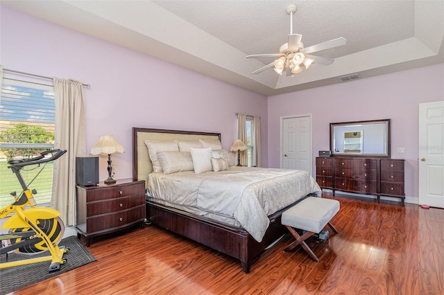 bedroom featuring ceiling fan, a textured ceiling, a tray ceiling, and dark hardwood / wood-style floors