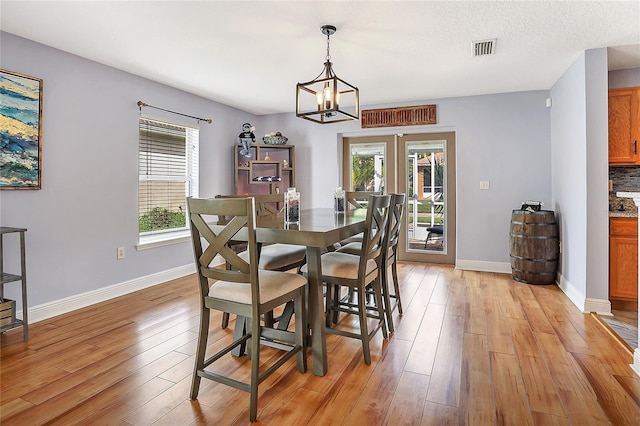 dining space featuring an inviting chandelier, light wood-type flooring, a textured ceiling, and plenty of natural light