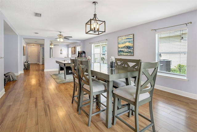 dining area with ceiling fan with notable chandelier, light wood-type flooring, and a healthy amount of sunlight