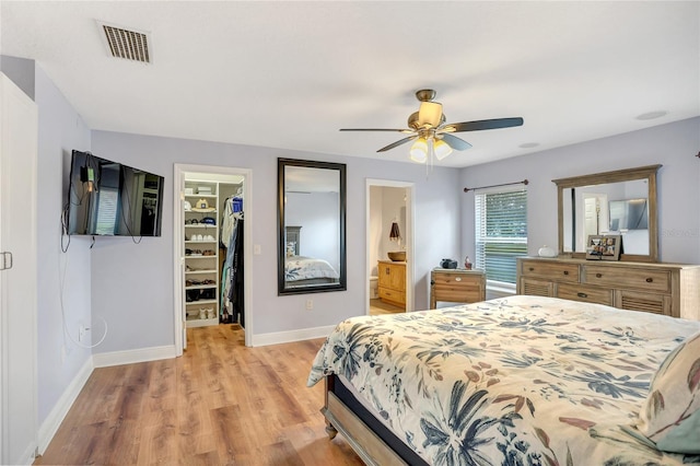 bedroom featuring ceiling fan, a closet, a spacious closet, light wood-type flooring, and ensuite bath