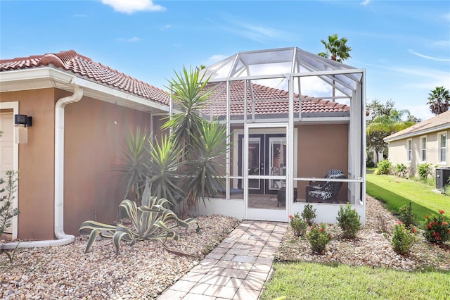 rear view of house with a sunroom, glass enclosure, and a lawn