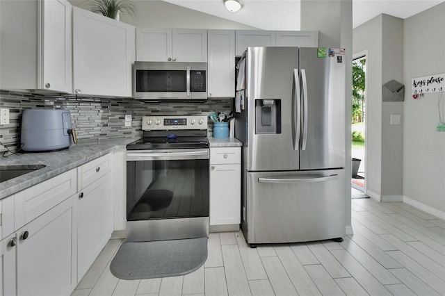 kitchen featuring decorative backsplash, light stone counters, white cabinets, stainless steel appliances, and light wood-type flooring