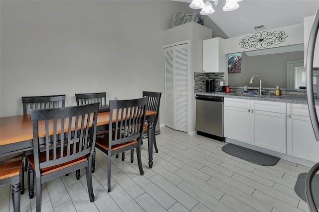 kitchen with sink, stainless steel dishwasher, white cabinetry, light stone countertops, and vaulted ceiling