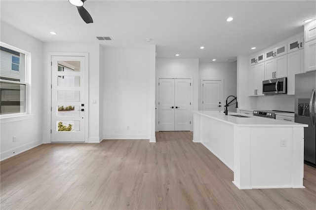 kitchen with white cabinetry, sink, stainless steel appliances, an island with sink, and light hardwood / wood-style floors