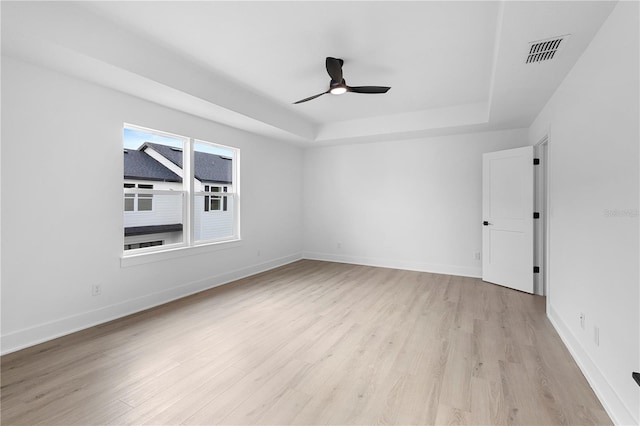 empty room featuring a tray ceiling, ceiling fan, and light wood-type flooring