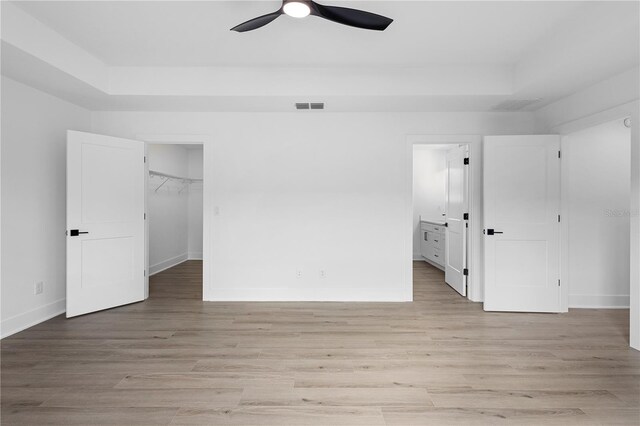 unfurnished bedroom with light wood-type flooring, a walk in closet, ensuite bath, and ceiling fan