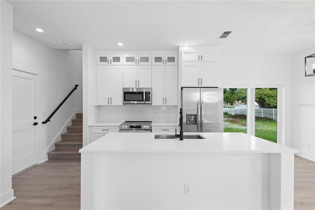 kitchen featuring white cabinets, stainless steel appliances, a kitchen island with sink, and light hardwood / wood-style floors