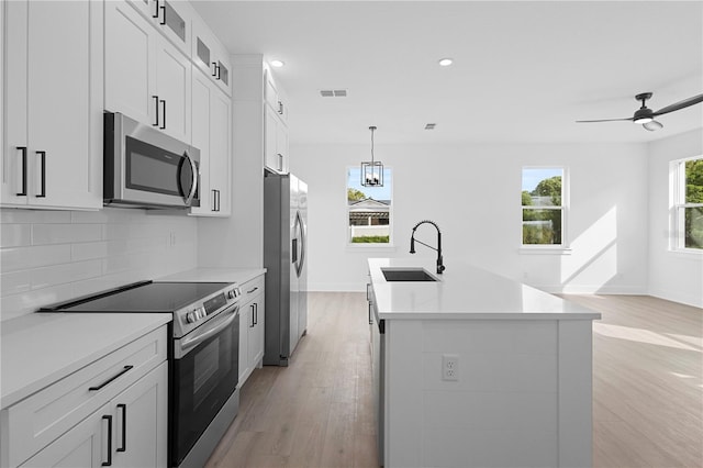 kitchen with sink, light hardwood / wood-style floors, a center island with sink, white cabinets, and appliances with stainless steel finishes