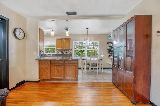 kitchen featuring tasteful backsplash, light wood-type flooring, pendant lighting, a notable chandelier, and sink