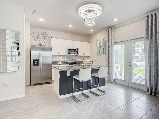 kitchen with an island with sink, stainless steel appliances, white cabinets, dark stone countertops, and a kitchen bar