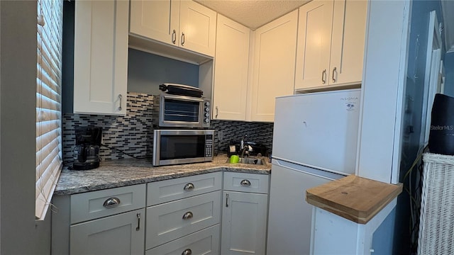 kitchen with light stone counters, white cabinets, tasteful backsplash, white fridge, and a textured ceiling