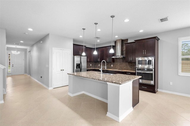 kitchen featuring sink, a kitchen island with sink, backsplash, wall chimney exhaust hood, and appliances with stainless steel finishes