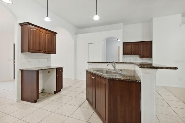 kitchen with dark stone counters, dark brown cabinetry, decorative light fixtures, sink, and light tile patterned floors