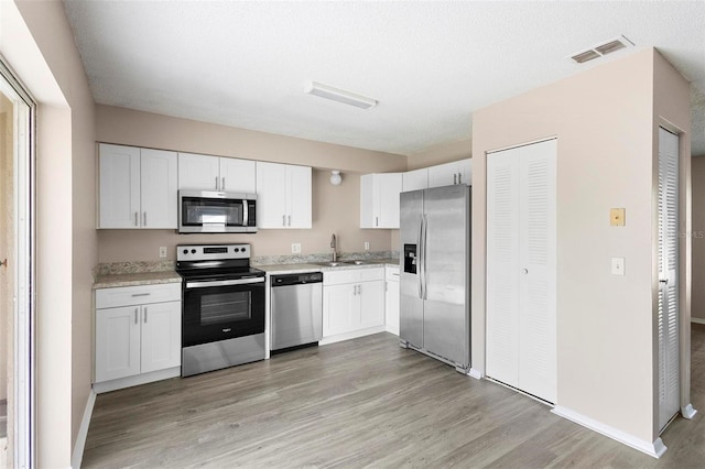 kitchen featuring white cabinets, stainless steel appliances, light wood-type flooring, and sink