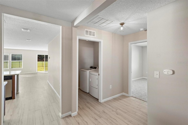 hallway with a textured ceiling, separate washer and dryer, and light hardwood / wood-style flooring