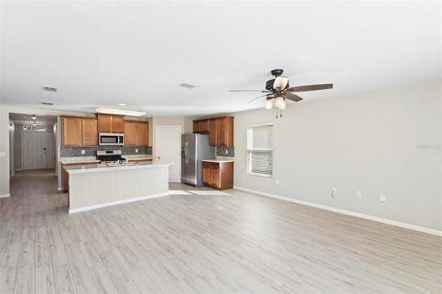 kitchen with an island with sink, ceiling fan, stainless steel appliances, light hardwood / wood-style flooring, and backsplash