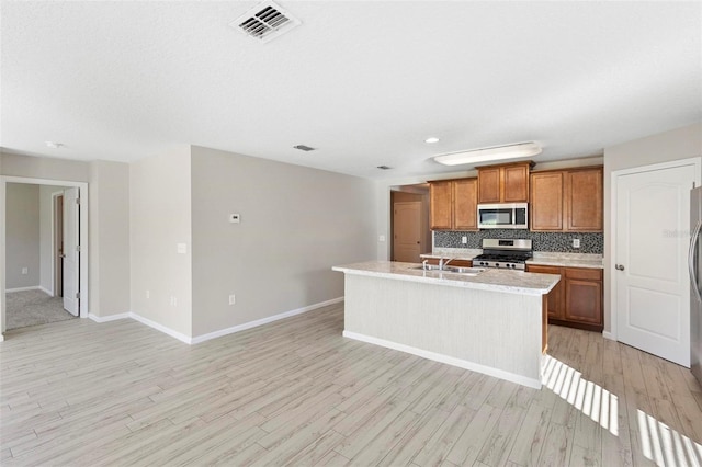 kitchen with a kitchen island with sink, appliances with stainless steel finishes, light wood-type flooring, and sink