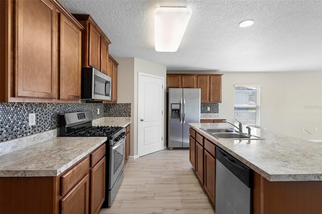 kitchen with stainless steel appliances, sink, light hardwood / wood-style floors, a center island with sink, and a textured ceiling