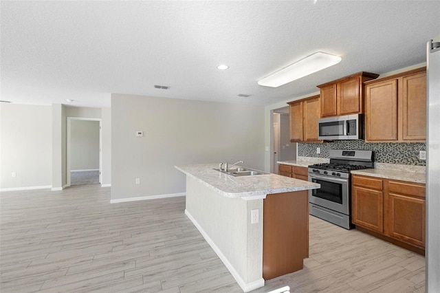 kitchen with light wood-type flooring, a center island with sink, sink, stainless steel appliances, and a textured ceiling