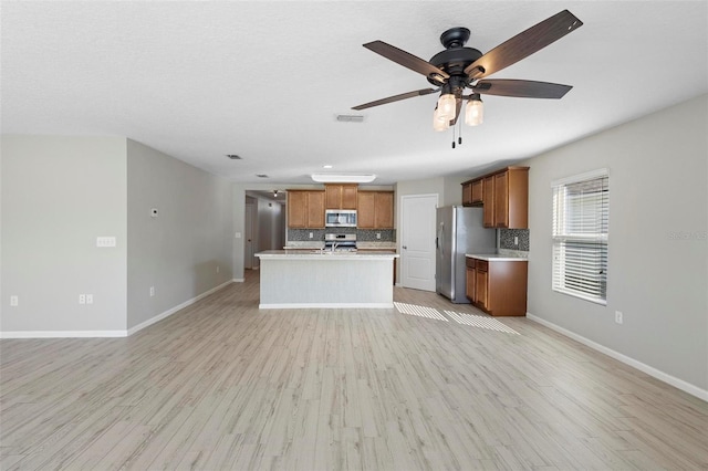 kitchen with a kitchen island, appliances with stainless steel finishes, decorative backsplash, and light hardwood / wood-style flooring