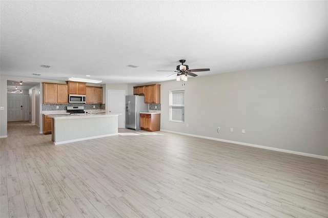 kitchen with appliances with stainless steel finishes, ceiling fan, decorative backsplash, and light hardwood / wood-style floors