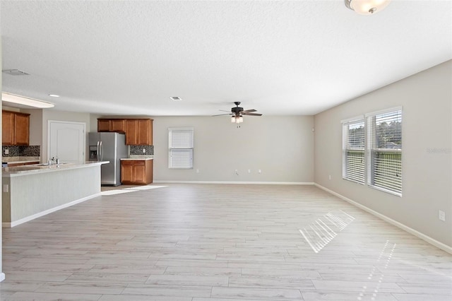 unfurnished living room featuring ceiling fan, sink, light hardwood / wood-style floors, and a textured ceiling