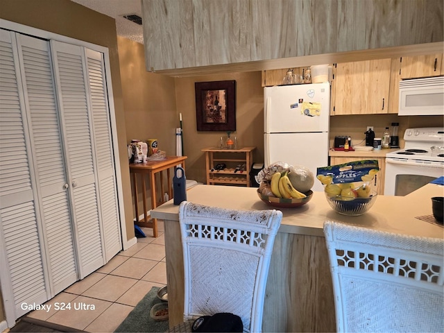 kitchen featuring light tile patterned floors, light brown cabinetry, and white appliances