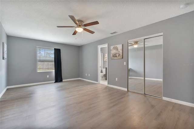 unfurnished bedroom with ceiling fan, hardwood / wood-style flooring, connected bathroom, a textured ceiling, and a closet