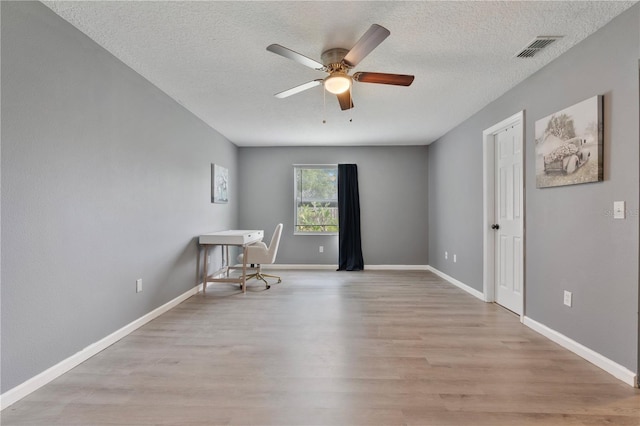 spare room featuring ceiling fan, light wood-type flooring, and a textured ceiling