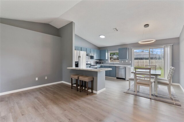 kitchen featuring appliances with stainless steel finishes, lofted ceiling, a kitchen bar, decorative light fixtures, and kitchen peninsula