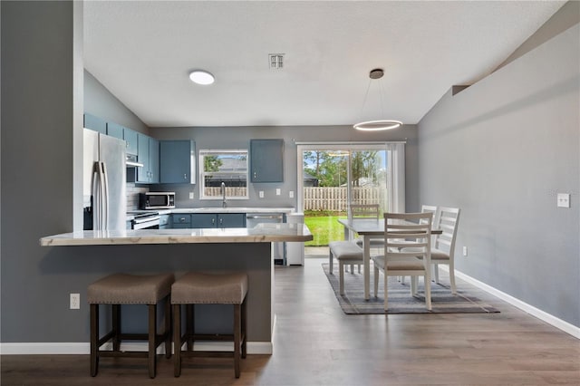 kitchen with vaulted ceiling, stainless steel appliances, a kitchen bar, and blue cabinetry