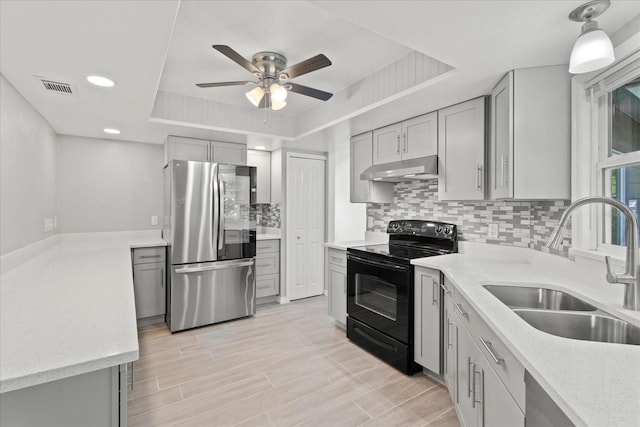 kitchen with a tray ceiling, stainless steel refrigerator, gray cabinets, black range with electric cooktop, and sink