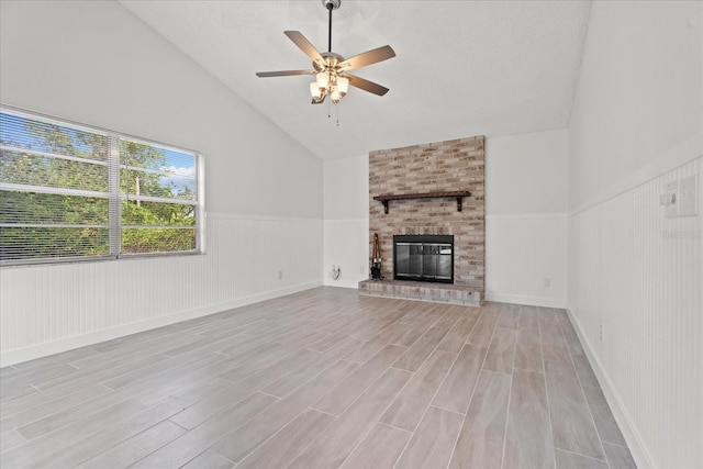 unfurnished living room with ceiling fan, a textured ceiling, a brick fireplace, vaulted ceiling, and light hardwood / wood-style floors