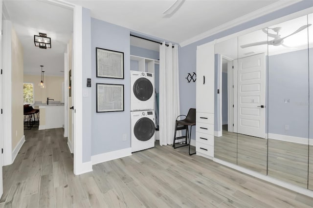 laundry area featuring crown molding, ceiling fan, stacked washer / drying machine, and light wood-type flooring