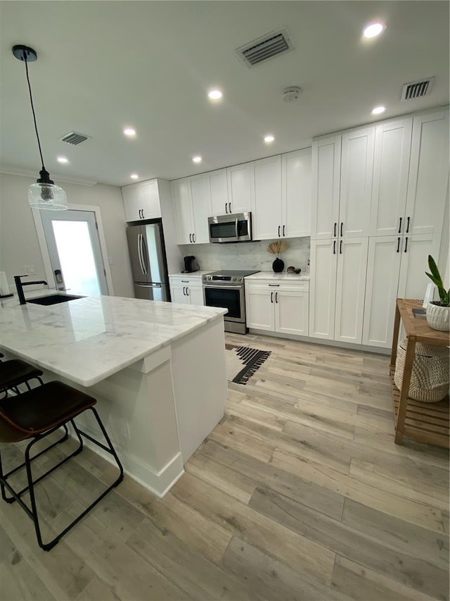 kitchen featuring appliances with stainless steel finishes, white cabinetry, hanging light fixtures, and light stone counters