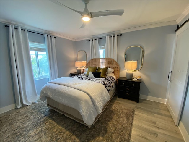 bedroom featuring hardwood / wood-style floors, ceiling fan, a barn door, and ornamental molding