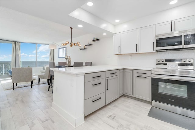 kitchen featuring kitchen peninsula, decorative light fixtures, white cabinetry, appliances with stainless steel finishes, and a water view